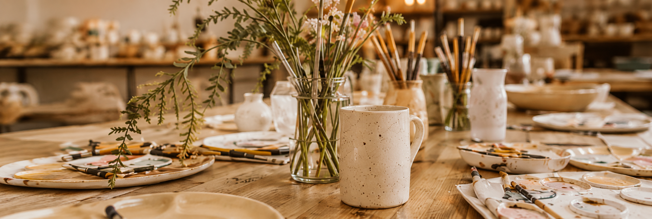 Table d'atelier avec céramiques, pinceaux et fleurs séchées